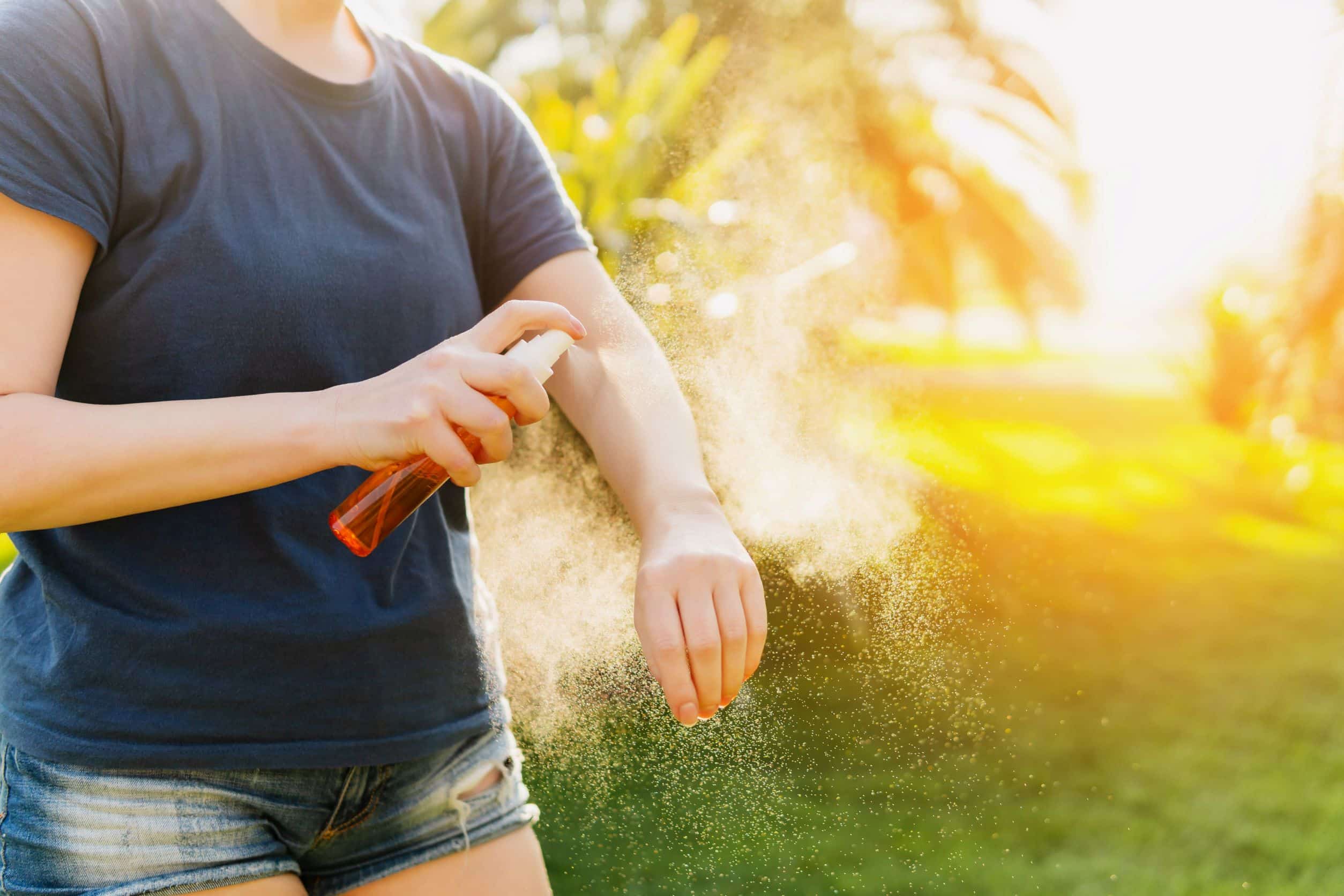 Woman spraying her arm with bug spray.