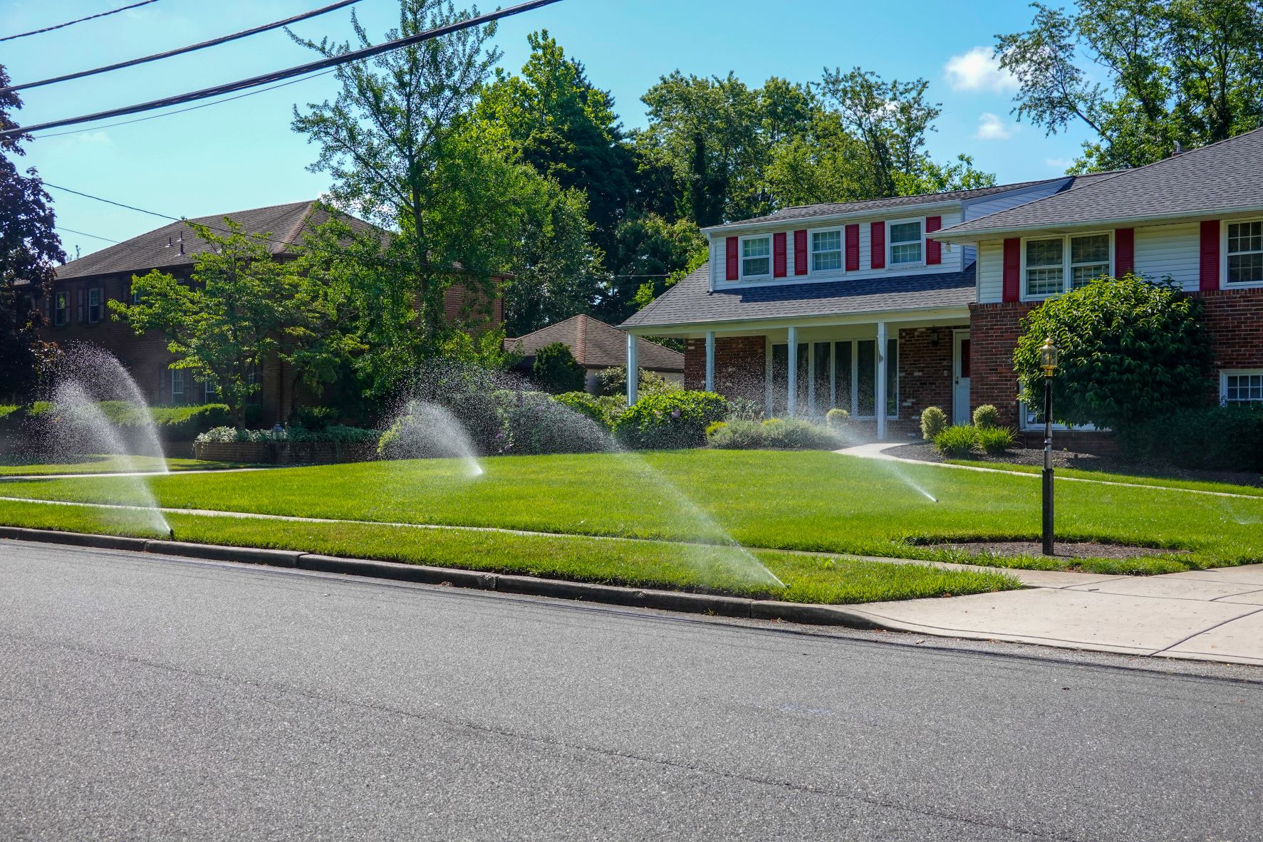 Two story brick house with multiple sprinklers spraying the yard.
